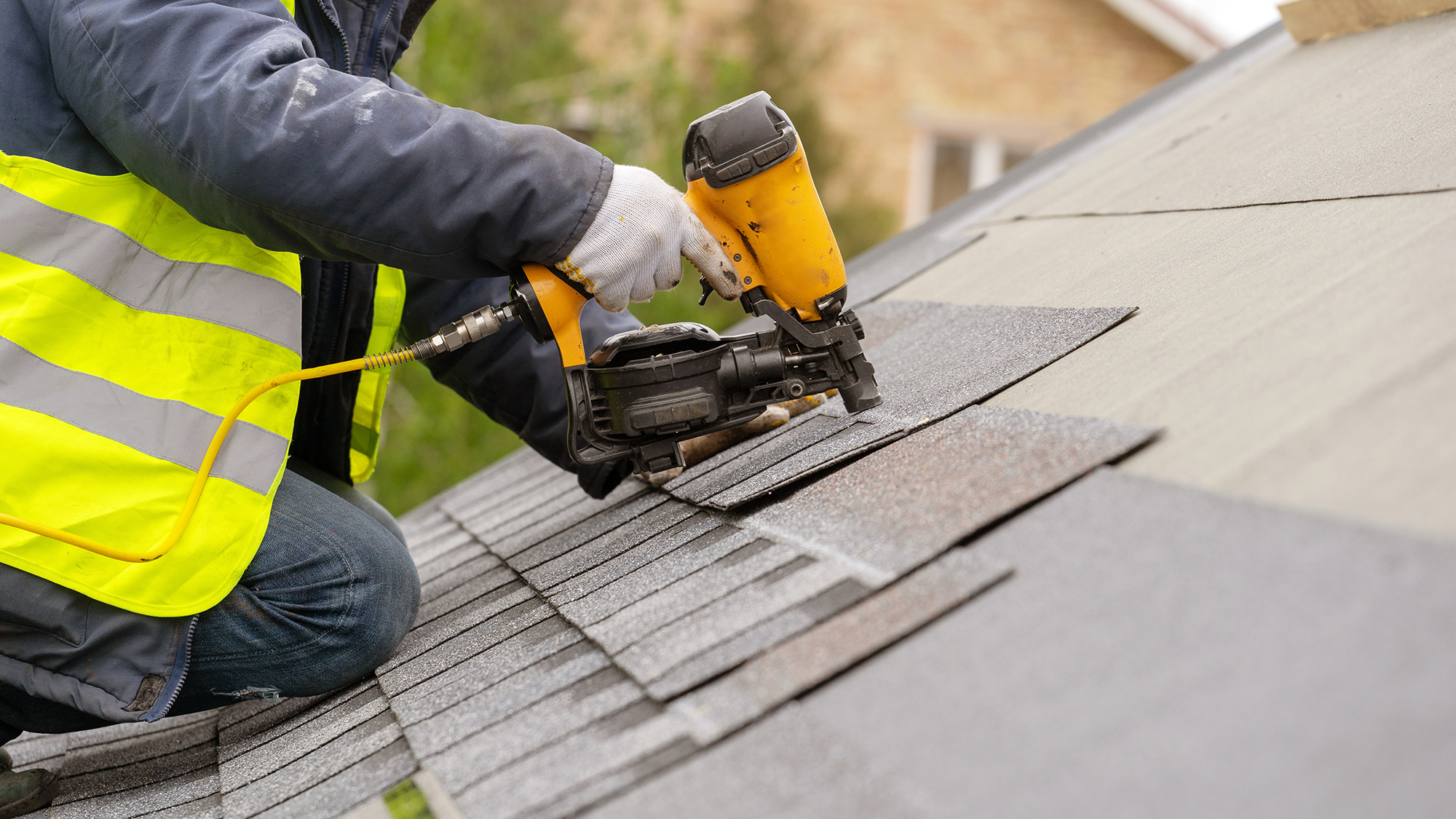 Roofer using a nail gun to install shingles on a residential roof